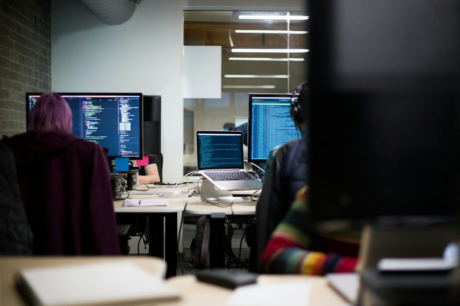 Developers working at rows of monitors showing code in an office